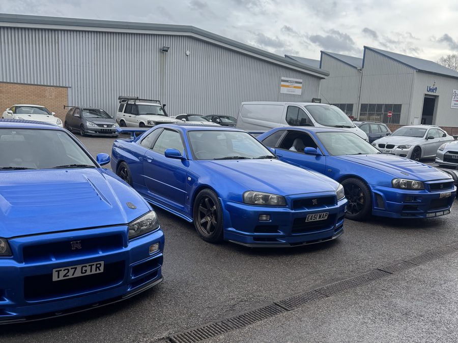 Three Bayside Blue Nissan Skyline R34 GT-Rs parked together outside the workshop